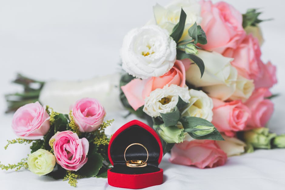 A close-up image featuring a bouquet of fresh flowers including pink, white, and cream roses, arranged with greenery. The bouquet is resting on a white surface with soft lighting highlighting the peta