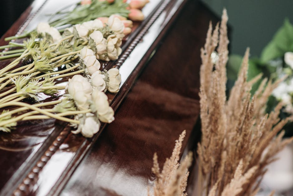 A close-up of a flower arrangement placed on a polished wooden surface, featuring delicate white carnations with slightly ruffled petals, complemented by light pink tulips with smooth petals, all arra